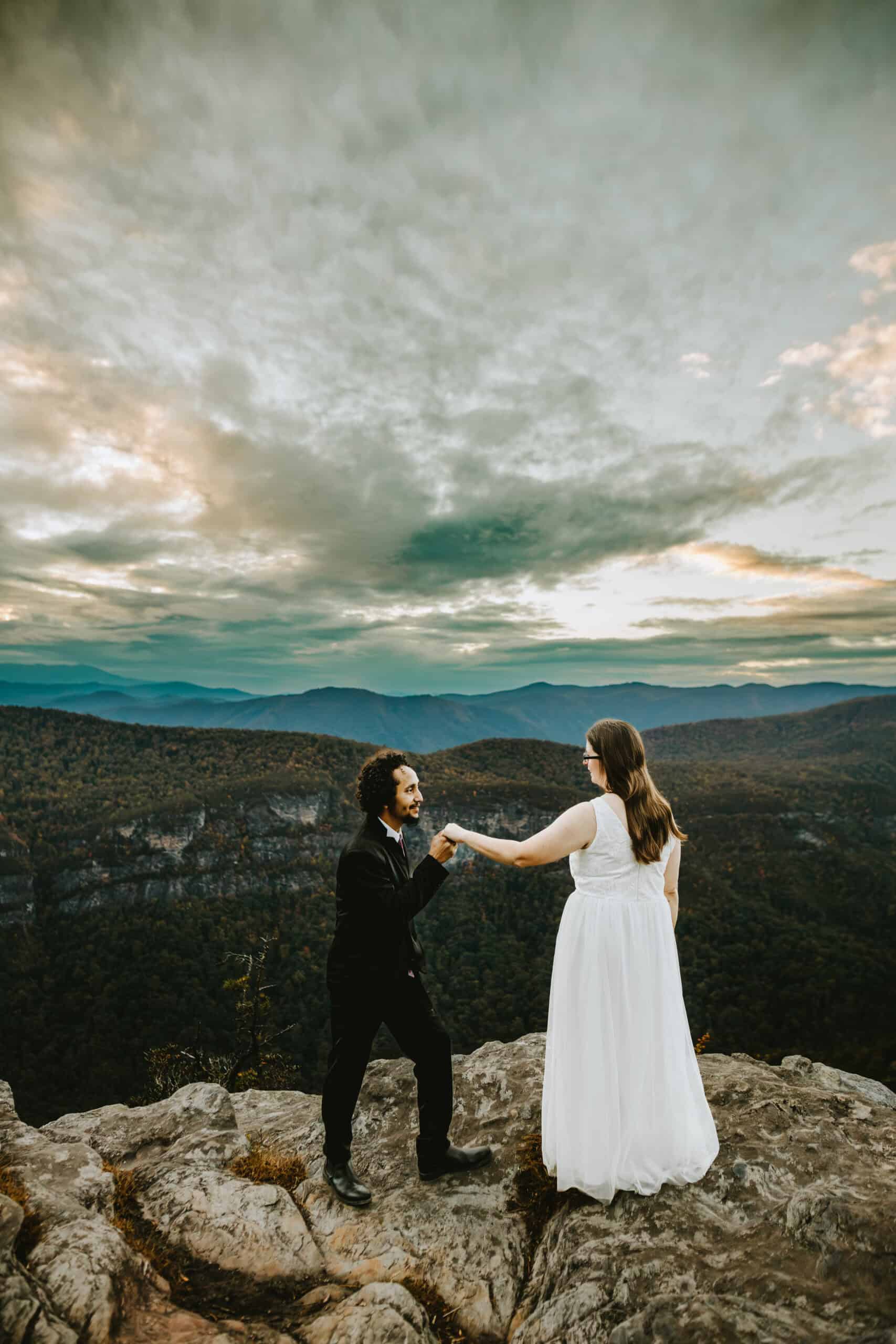 groom holding bride's hand on top of mountain