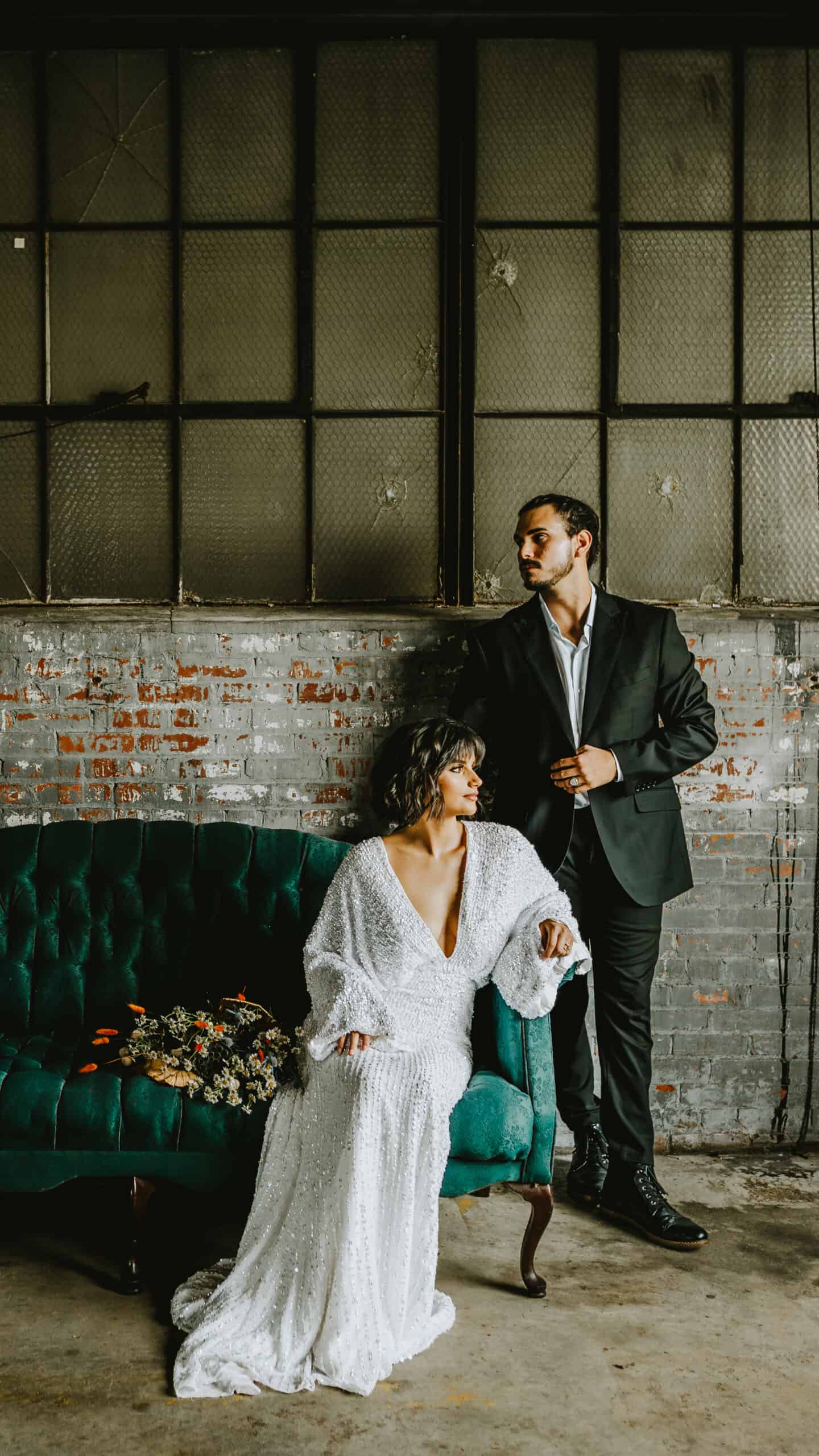 bride and groom in stunning wedding dresses posing in a photo studio on a green sofa