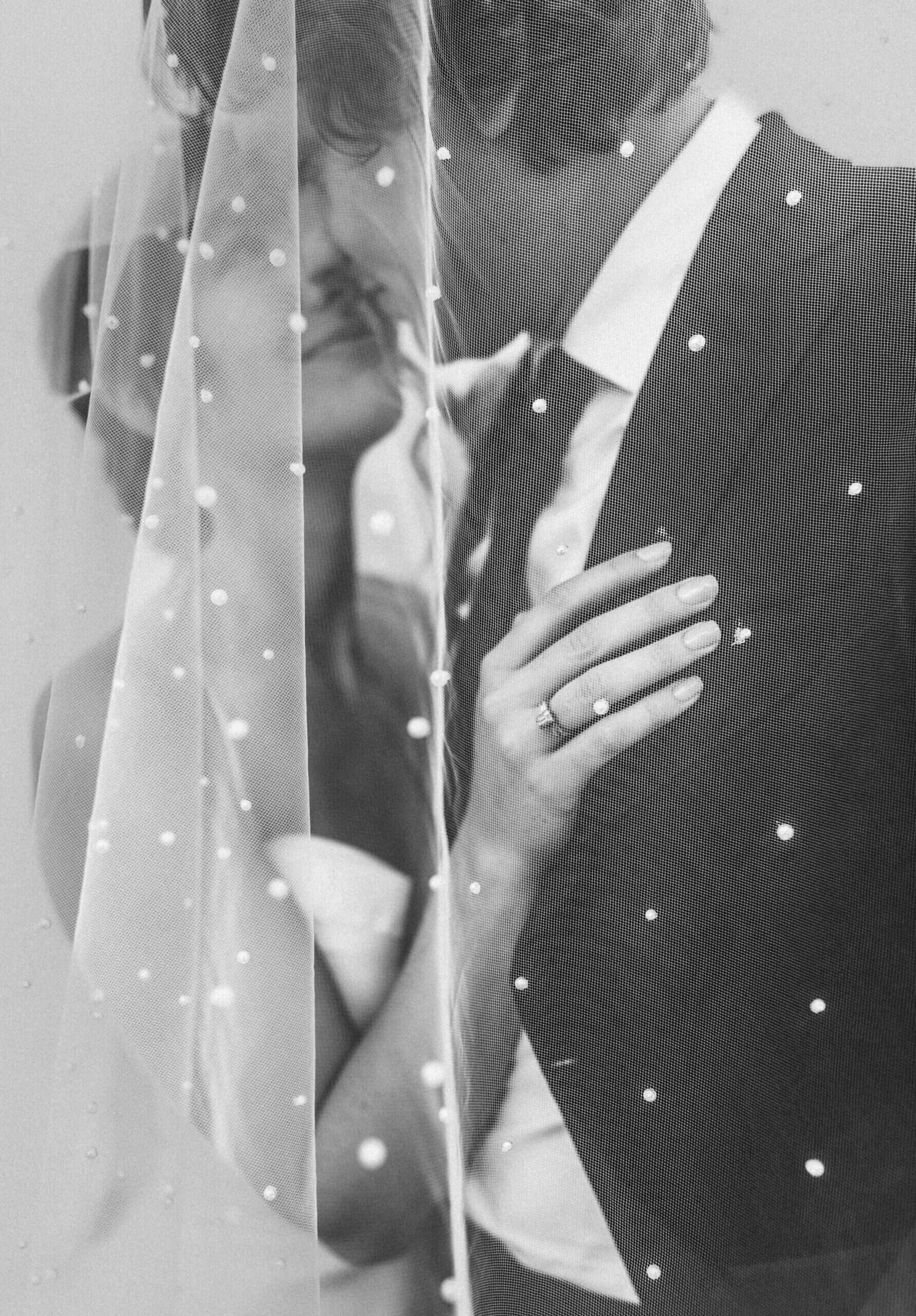 black and white photo of the bride and groom kissing under a veil
