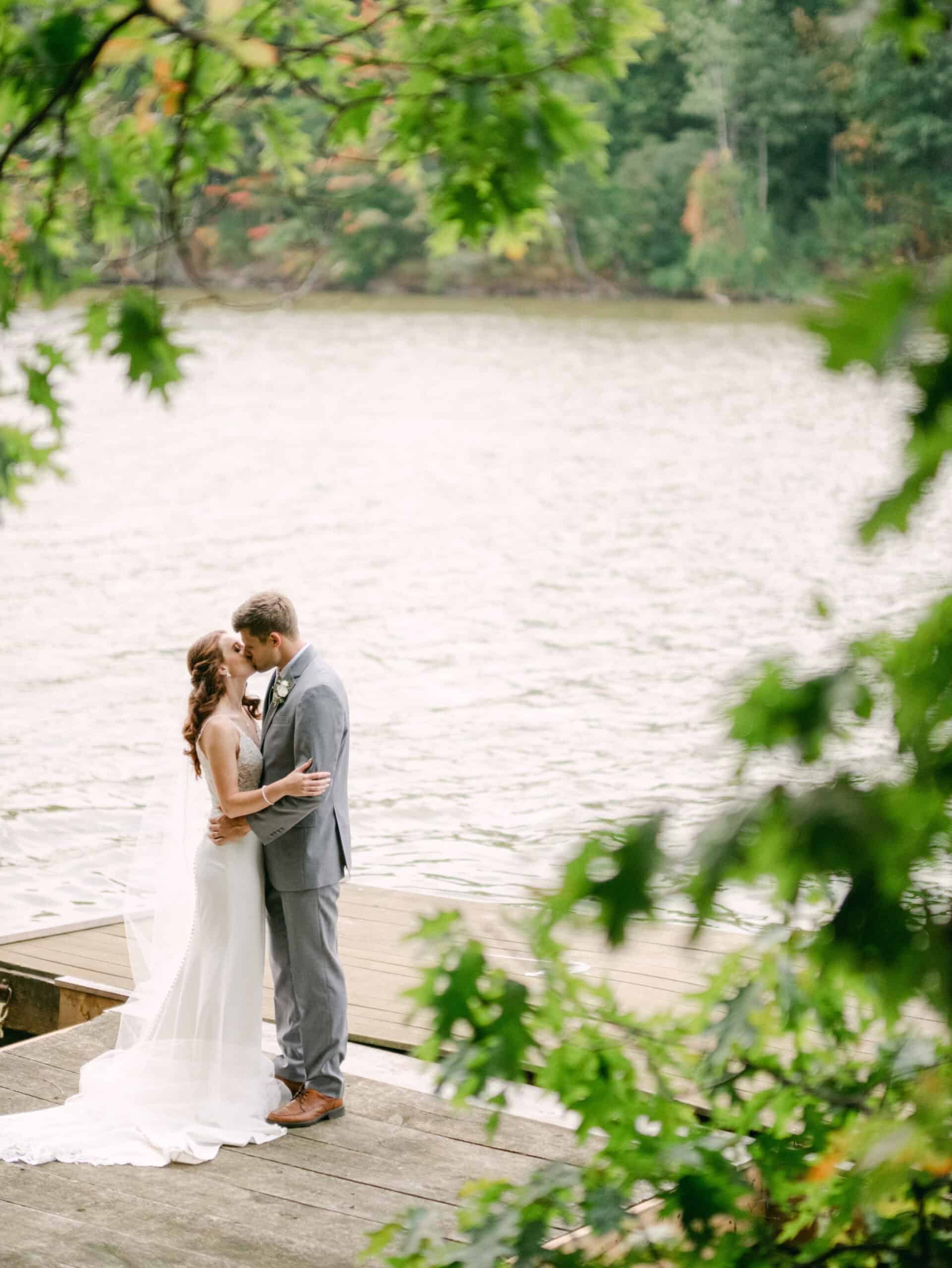 bride and groom kissing on a pier by the lake