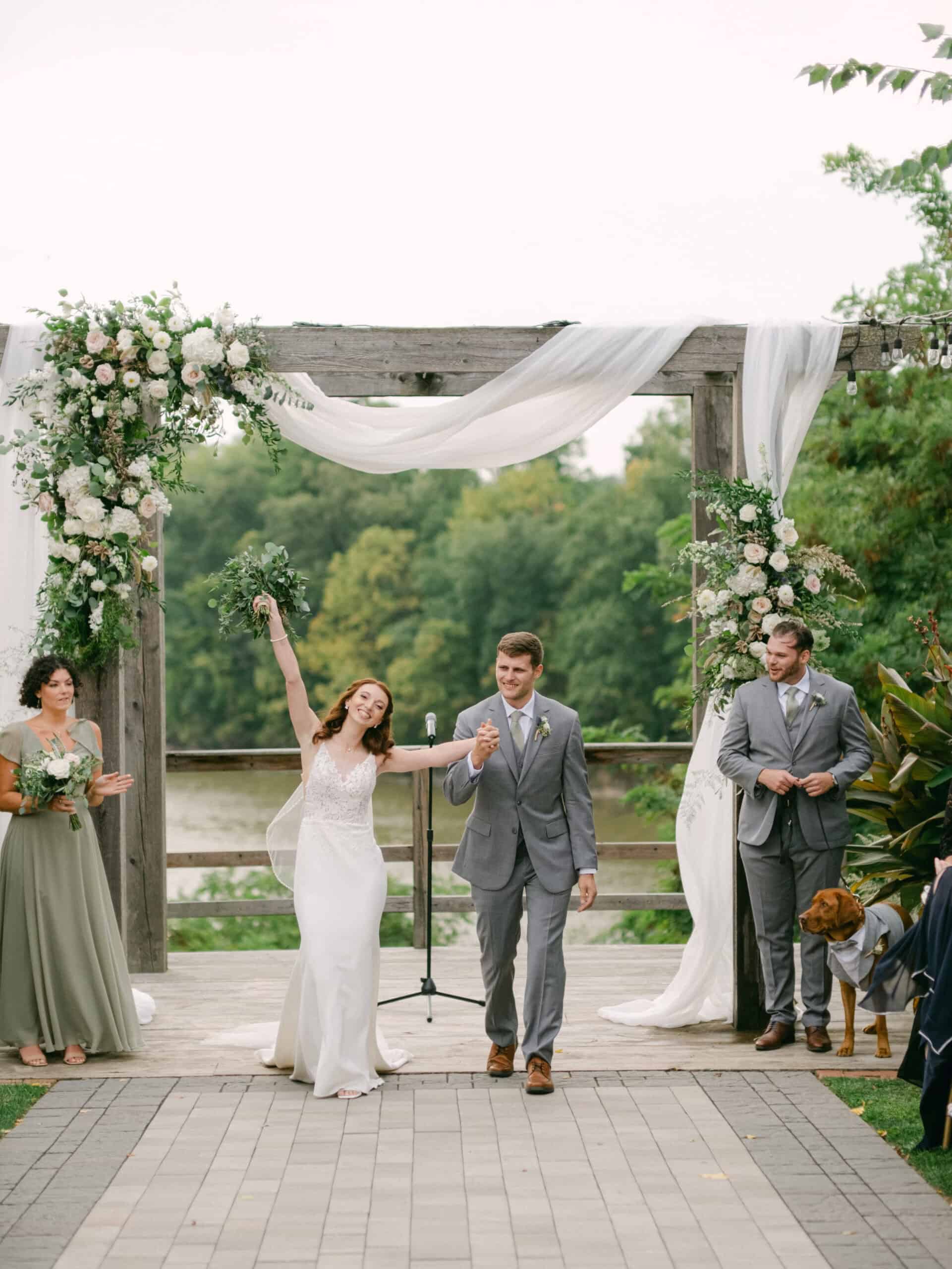 newlyweds rejoice holding hands near an arch with flowers