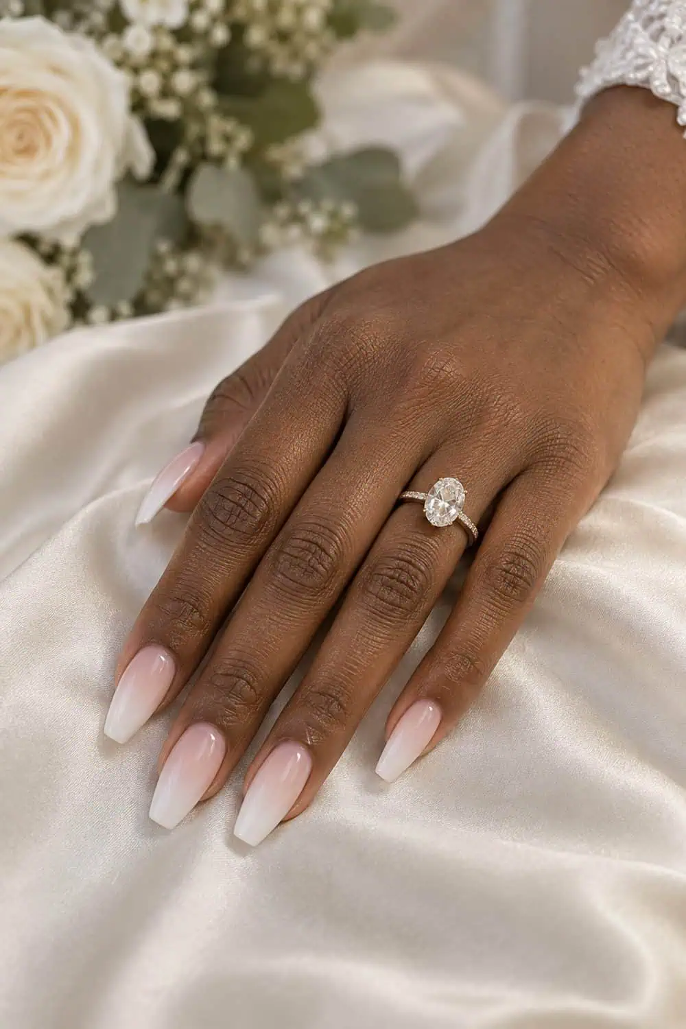 Bridal medium-deep brown hand with medium coffin nails fading from blush near cuticle to milky white tips, resting on cream satin