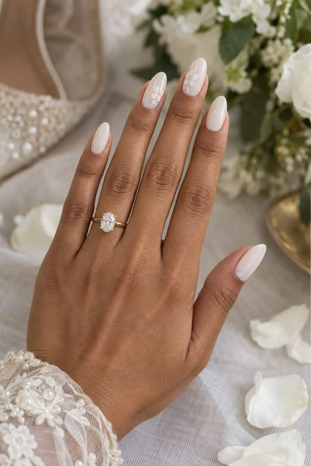 Bridal light-brown hand with medium almond nails, milky white polish and small white painted flowers on two accent nails, real white petals nearby