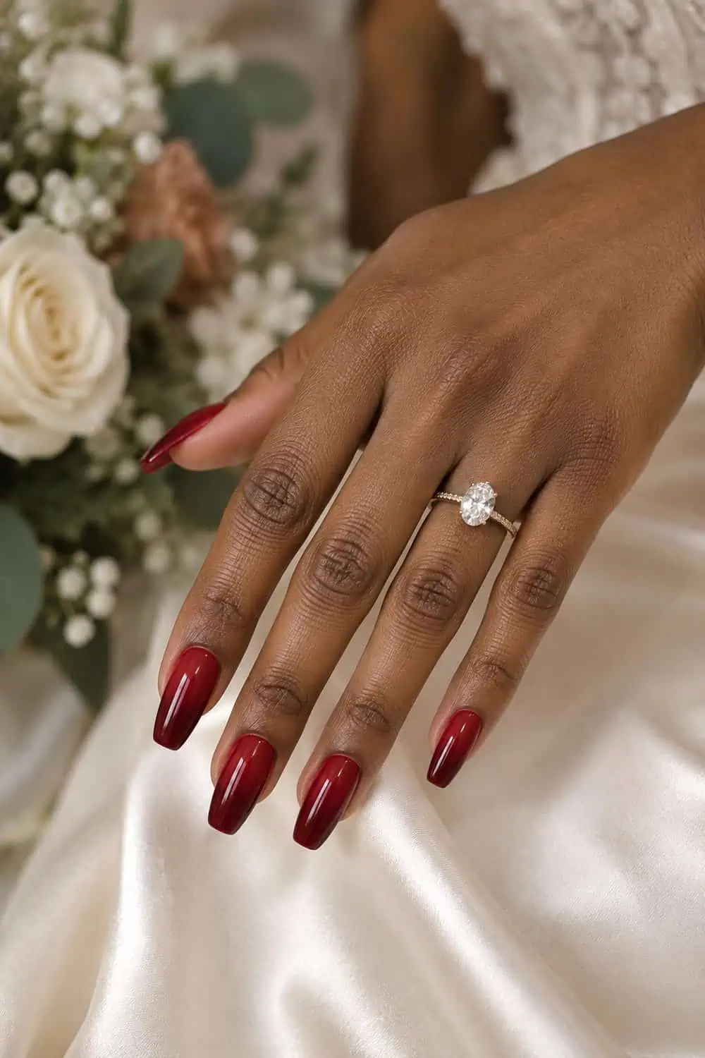Bridal medium-deep brown hand with medium coffin nails, red polish fading from scarlet near cuticles to burgundy-red tips, ivory satin