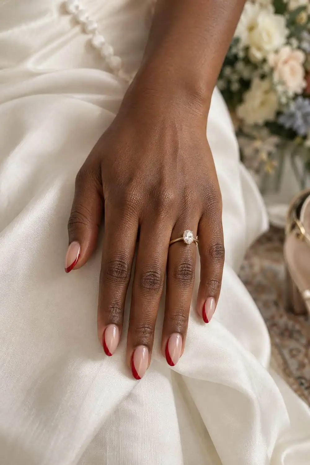 Bridal deep-brown hand with medium almond nails, sheer nude base and slim curved side-French line painted in cherry-red polish, ivory fabric