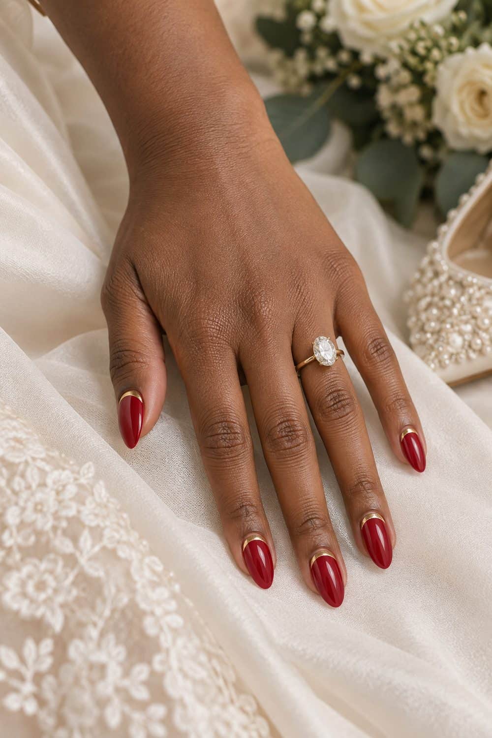 adult bride's medium-deep brown hand with medium almond nails painted scarlet red, thin gold curved cuff at each cuticle, ivory fabric