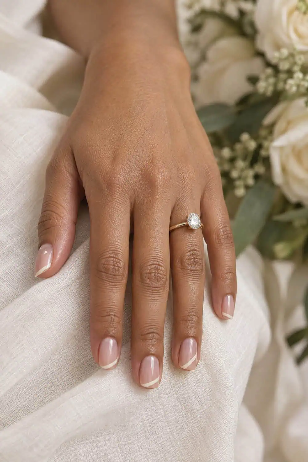 adult bride's light-brown hand with short square nails, sheer pink base and ultra-thin diagonal ivory tips, cream background