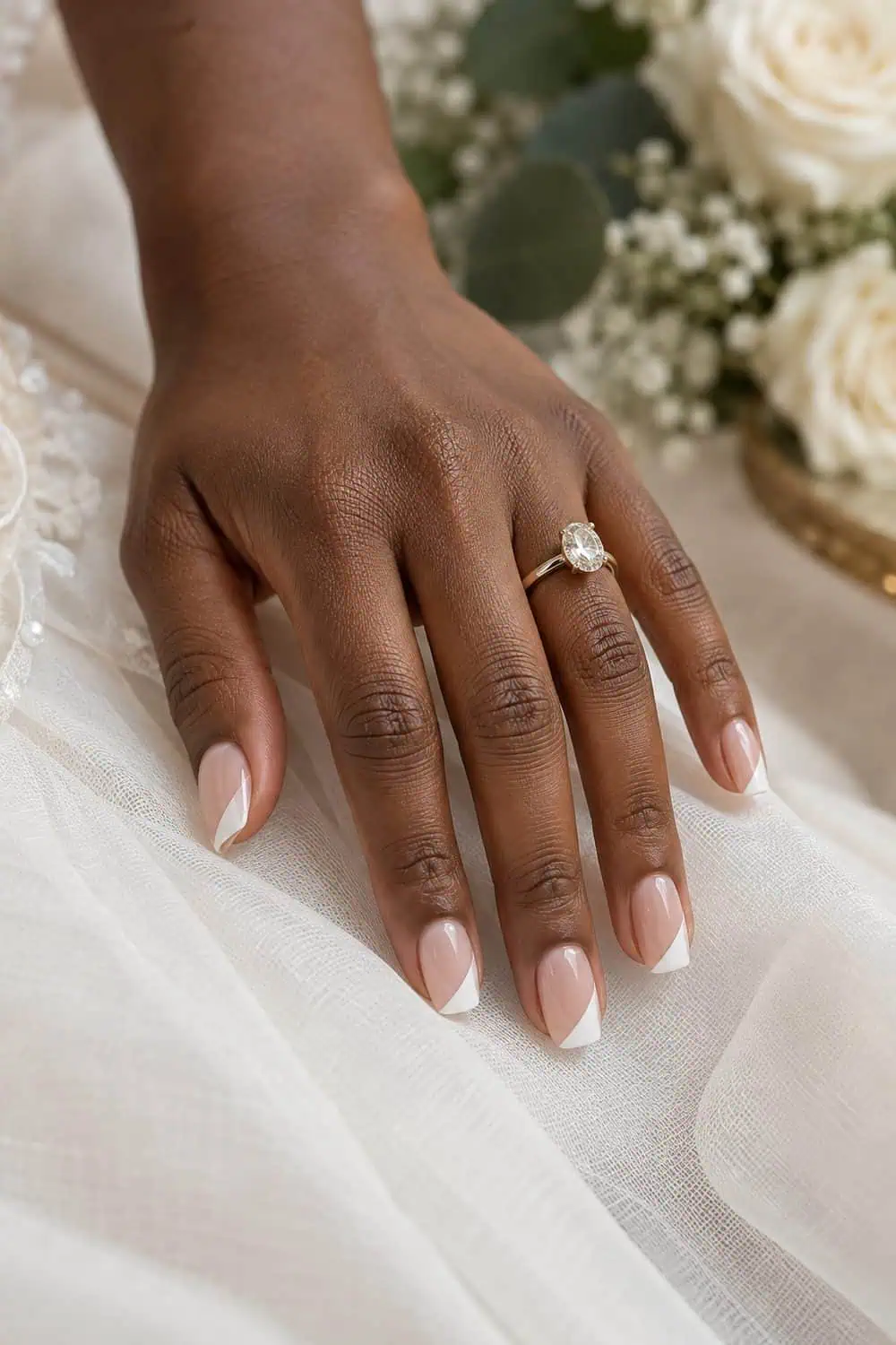 Bridal dark-brown hand with medium squoval nails, sheer nude base and one simple diagonal white tip on each nail, ivory fabric