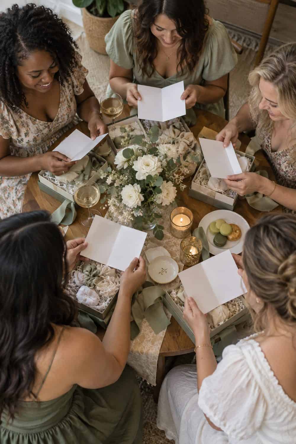 overhead view of bride and four diverse adult friends' hands around table with opened blank-inside cards, no readable text