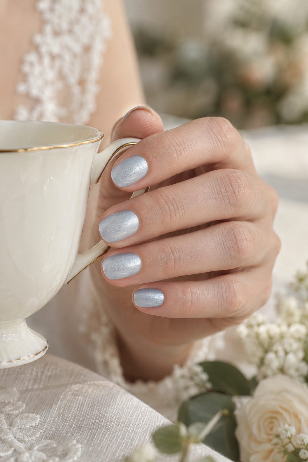 Bridal fair hand with short oval nails painted pearly pale blue, holding an ivory teacup