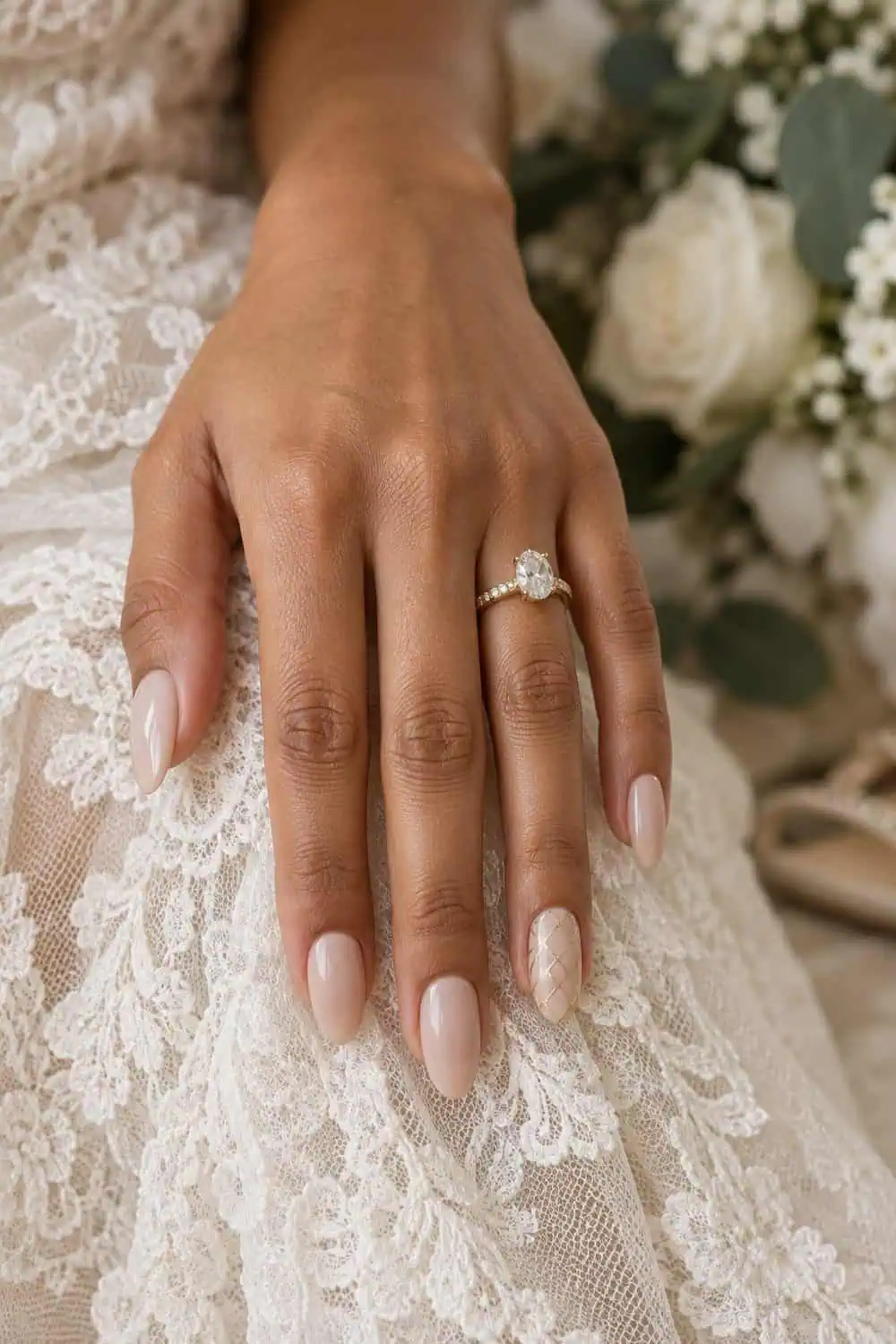 adult bride's light-brown hand with medium almond nails, sheer beige polish and fine gold lattice lines on one accent nail, cream lace nearby