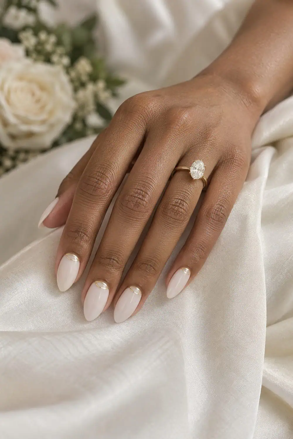 Bridal medium-brown hand with medium almond nails painted translucent milky white, thin gold curved cuff line at each cuticle, ivory silk