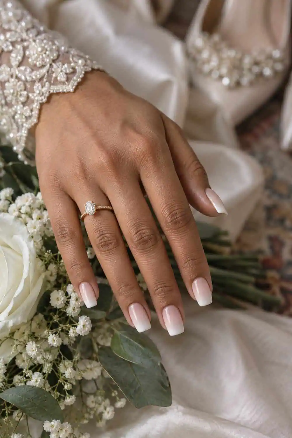 adult bride's South Asian hand with medium soft-square nails fading from translucent pink to pearl white, ivory satin