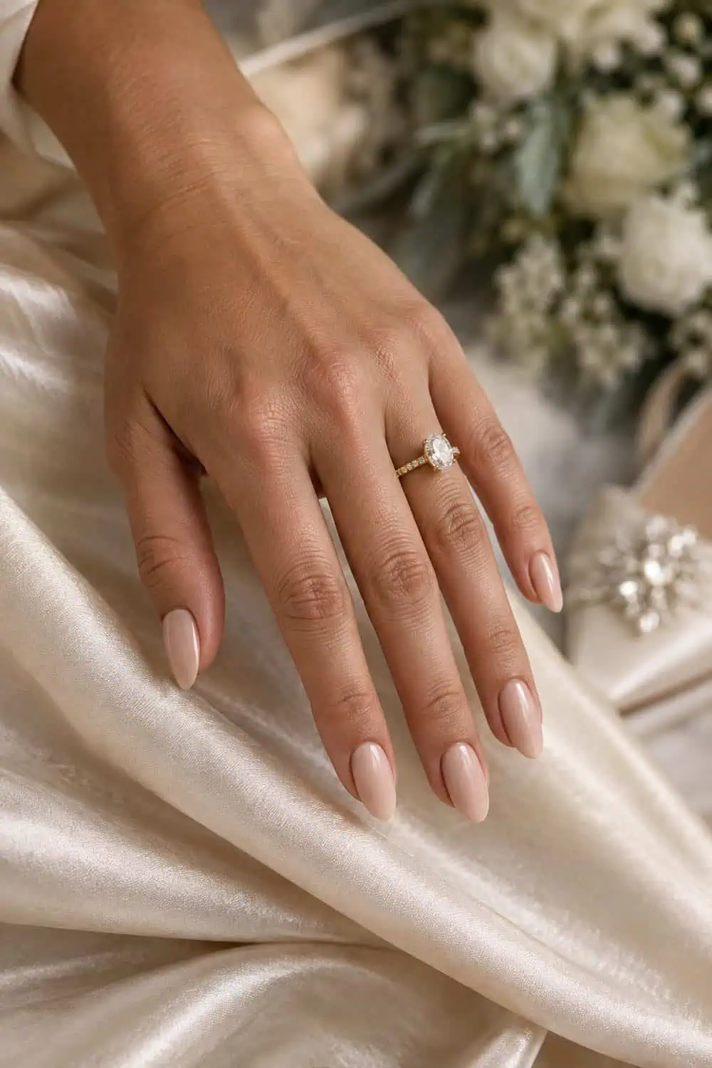 adult bride's warm tan hand with medium almond nails painted warm nude with a smooth satin finish, champagne fabric