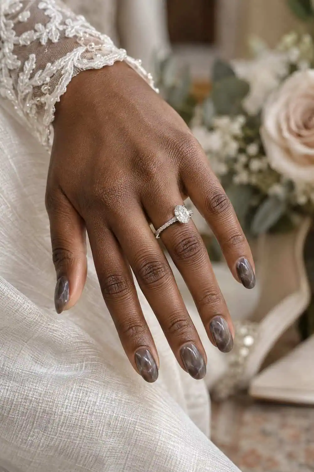 adult bride's deep-brown hand with medium oval nails, translucent smoky gray-brown quartz effect with sparse pale veins, silver ring