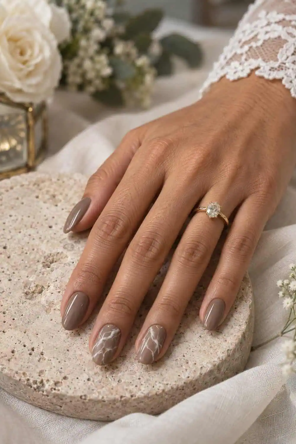 adult bride's olive-toned hand with medium oval nails, solid taupe polish with subtle cream marble lines on two accent nails, stone tray