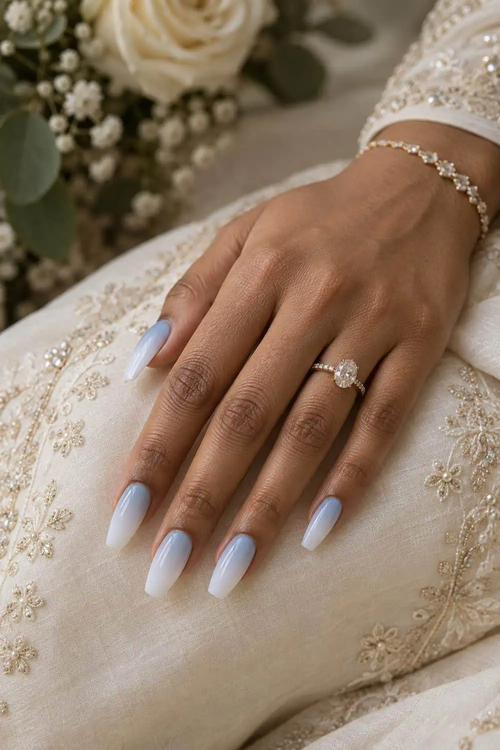 Bridal South Asian hand with medium coffin nails fading from pale blue near cuticles to soft white tips, ivory fabric