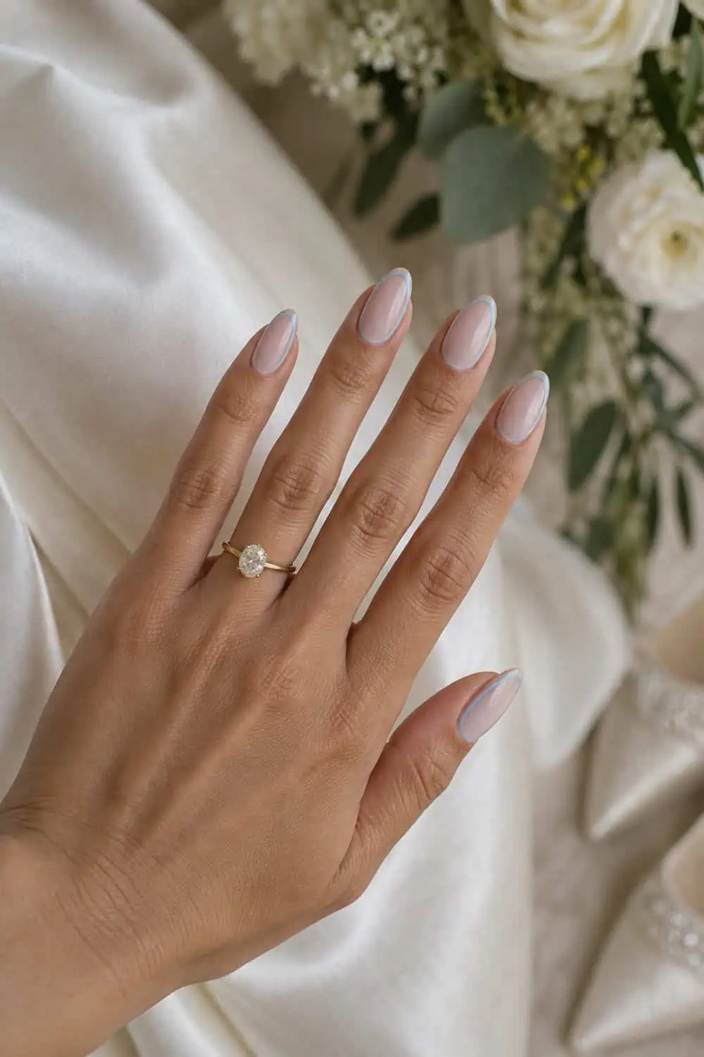 Bridal olive hand with medium almond nails, sheer nude centers and very thin soft-blue outline around each nail, ivory satin