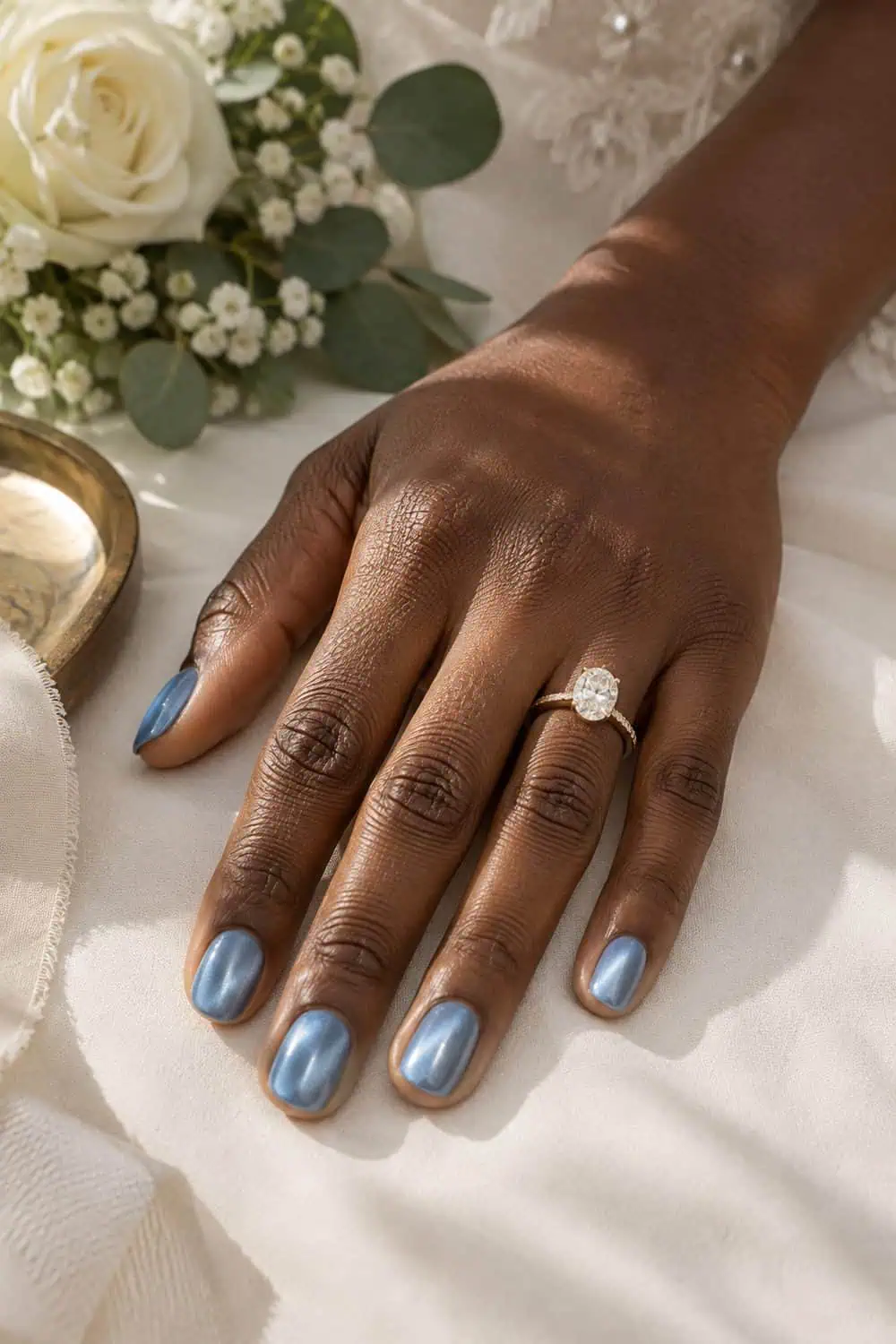 Bridal deep-brown hand with short rounded nails painted powder-blue magnetic velvet polish, soft light bands visible, ivory background