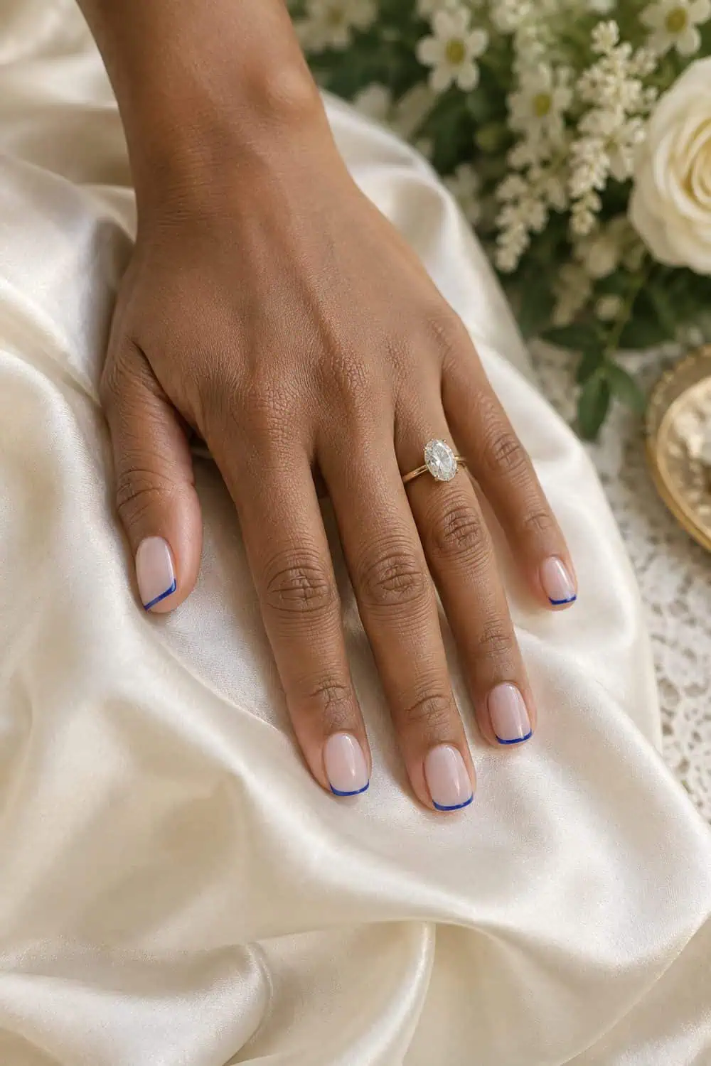 adult bride's medium-brown hand with short square nails, sheer nude base and ultra-thin cobalt-blue French tips, ivory silk