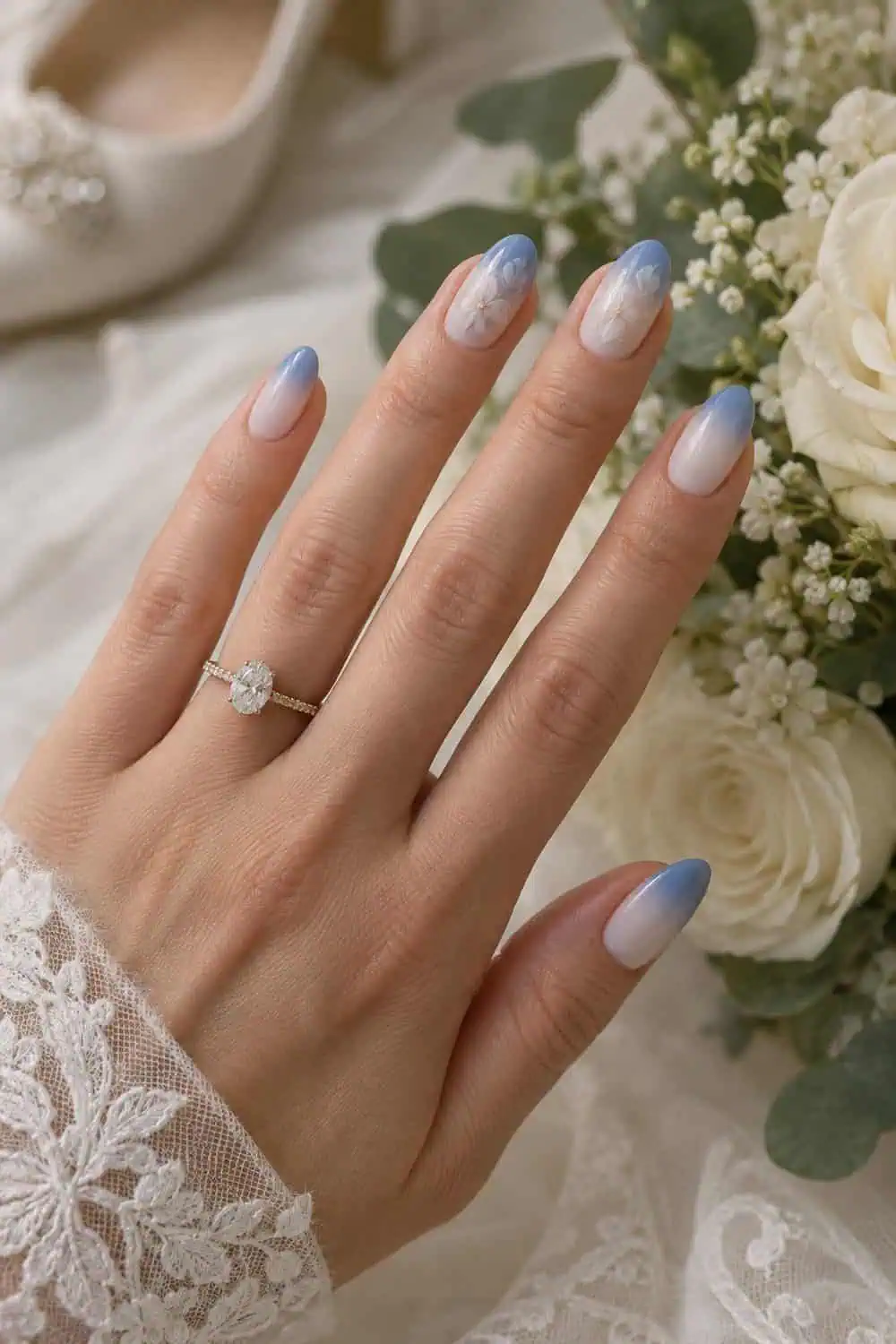 adult bride's fair hand with medium almond nails fading from cornflower blue tips to milky white near cuticles, cream flowers