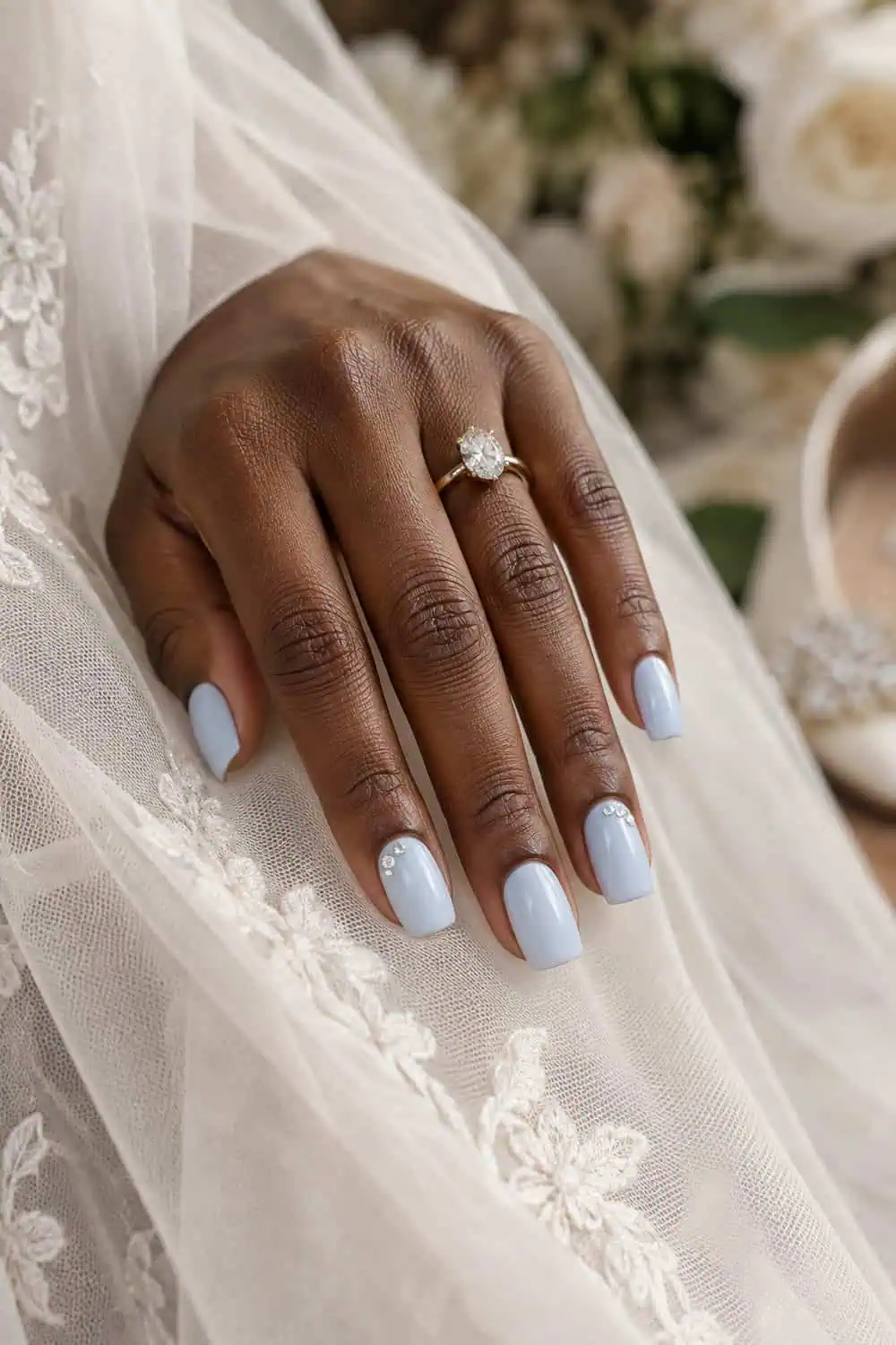 adult bride's deep-brown hand with medium square nails painted ice blue, tiny clear crystals on outer corners of two nails, cream veil fabric
