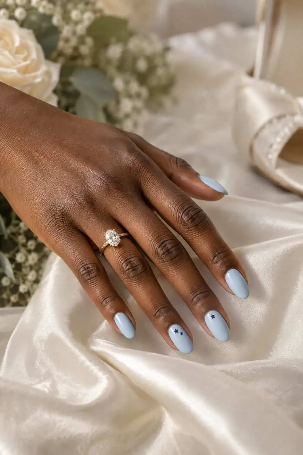 adult bride's dark-brown hand with medium oval nails painted pale blue, tiny navy stars on two accent nails only, ivory satin