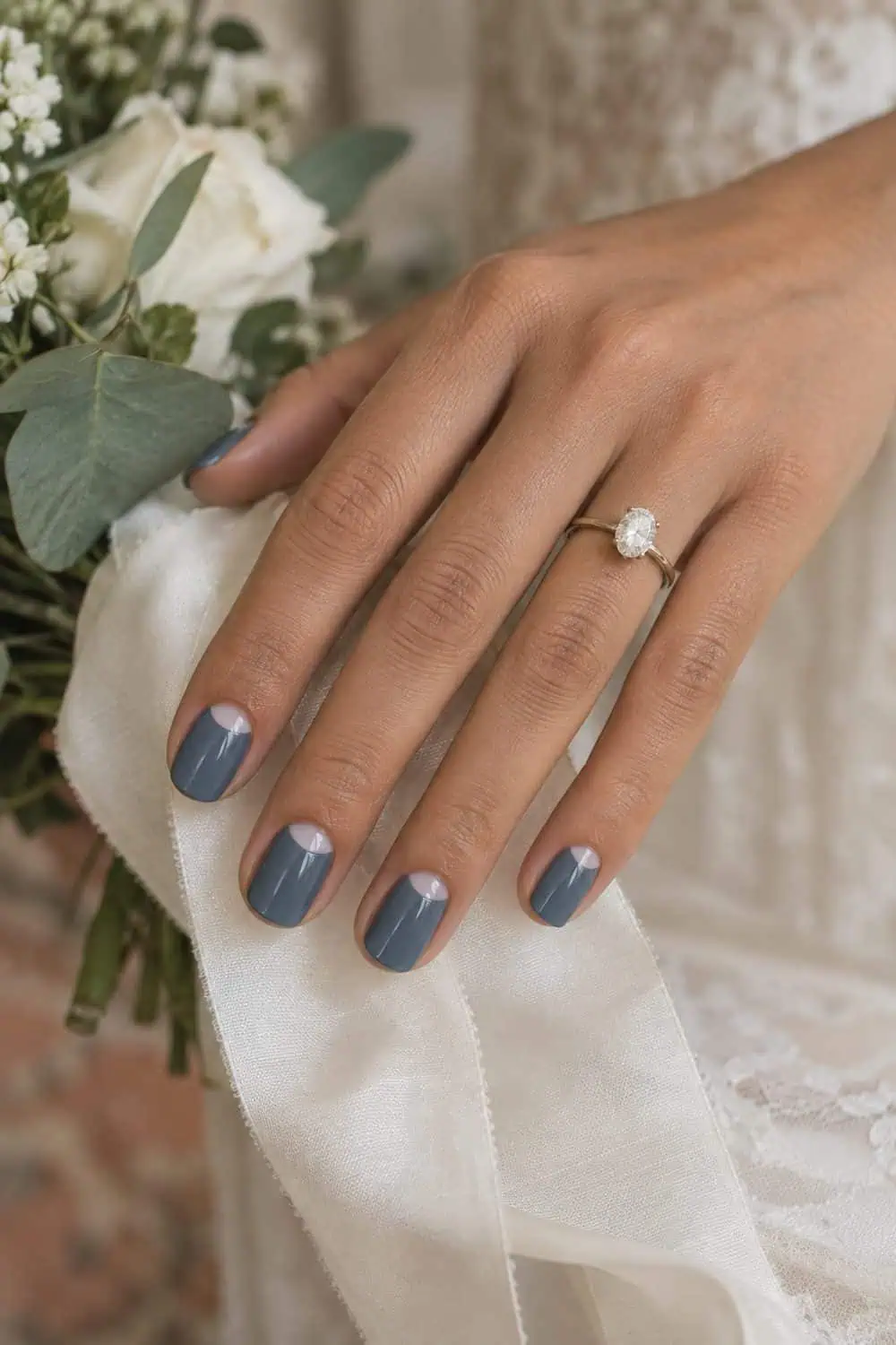 adult bride's warm tan hand with short squoval nails painted slate blue with small clear half-moons at cuticles, ivory ribbon