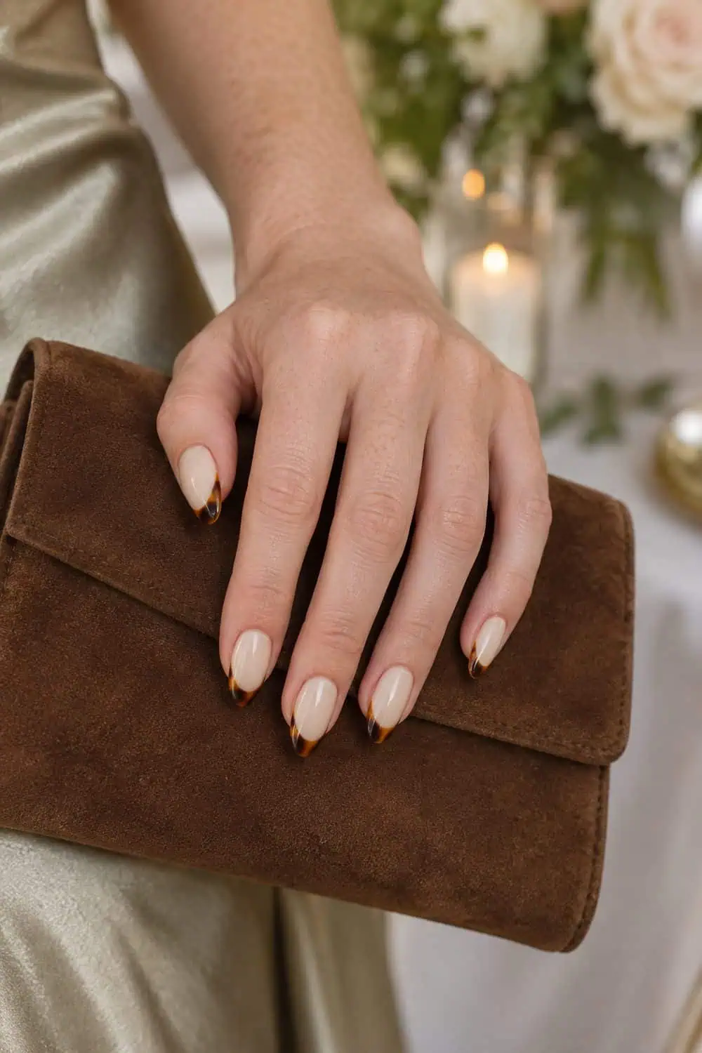 adult wedding attendee's fair freckled hand with medium almond nails, creamy beige base and narrow amber tortoiseshell French tips, brown clutch