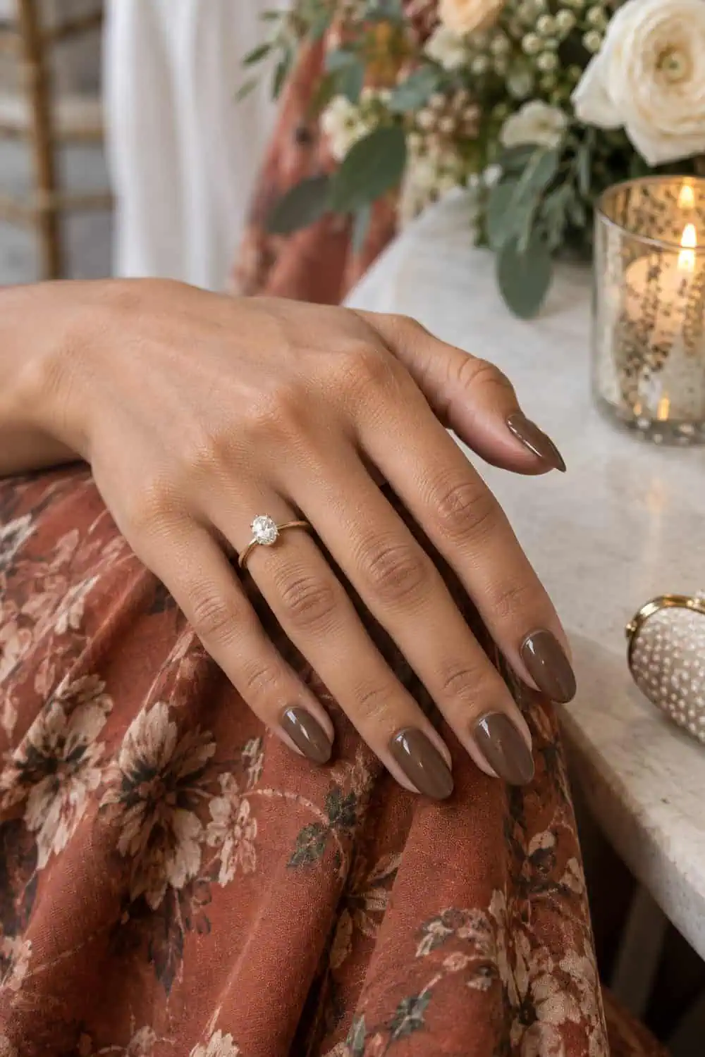 Wedding attendee olive hand with medium almond nails painted solid glossy mocha brown, rust floral fabric nearby
