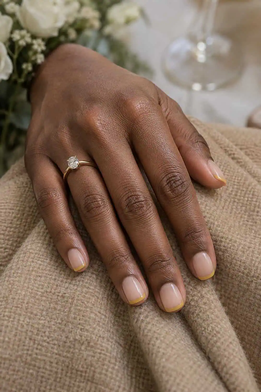 adult wedding attendee's dark-brown hand with short square nails, sheer beige base and ultra-thin muted mustard French tips, tan wool fabric