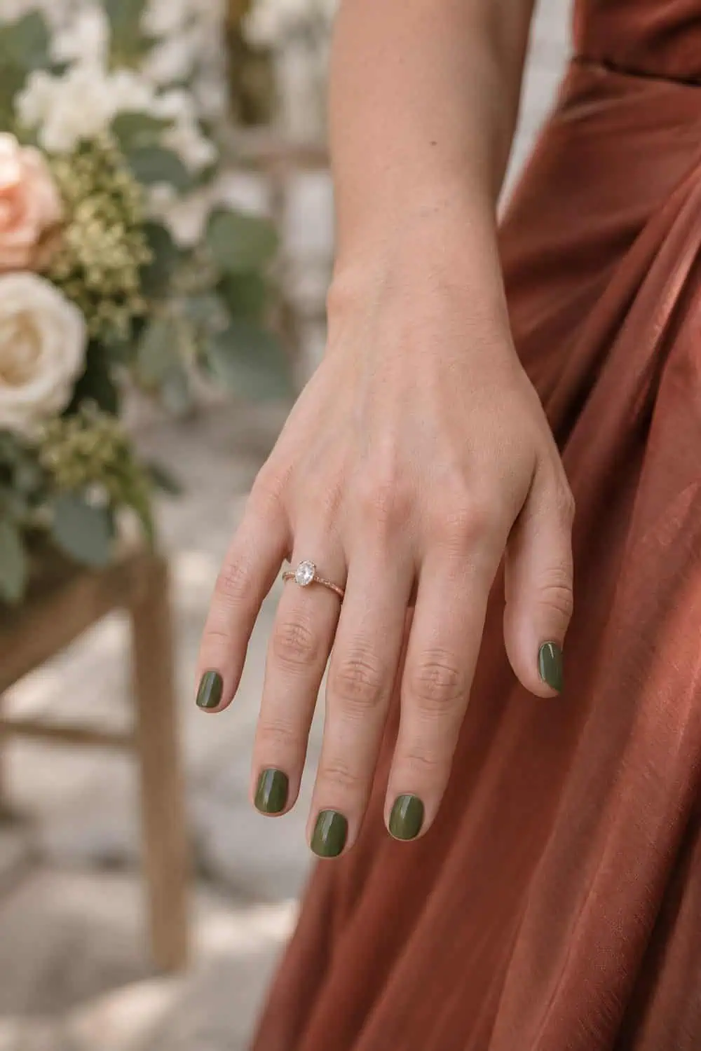 Wedding attendee fair hand with short rounded nails painted solid muted olive green, rust dress fabric nearby